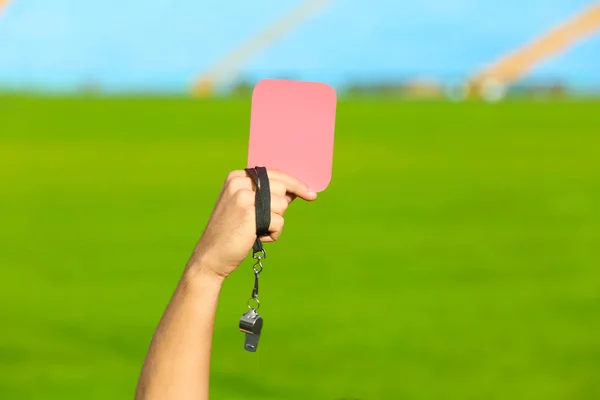 Football referee holding red card and whistle at stadium, closeup