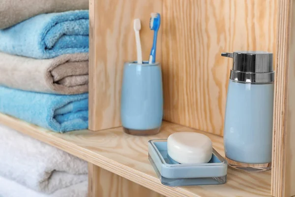 Dish with soap, bottle of shampoo and toothbrushes on wooden shelf