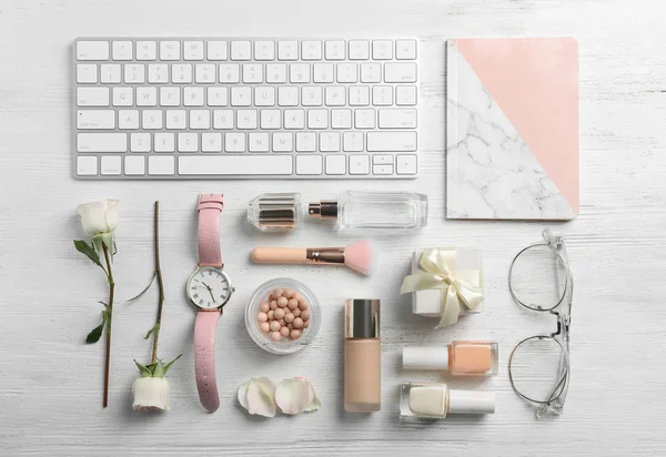 Flat lay composition with beautiful roses, cosmetics and keyboard on wooden background