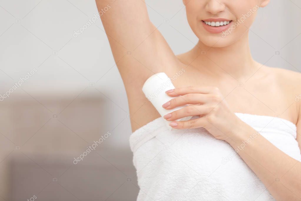 Beautiful young woman applying deodorant after shower on blurred background