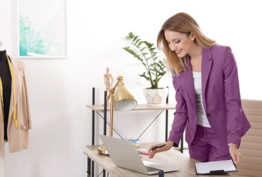 Güzel genç stilist Studio dizüstü bilgisayar ile çalışma. Moda giysiler