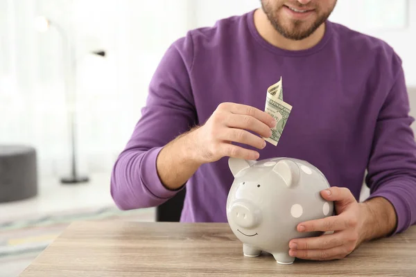 Jonge Man Brengen Geld Piggy Bank Aan Tafel Binnenshuis Ruimte — Stockfoto