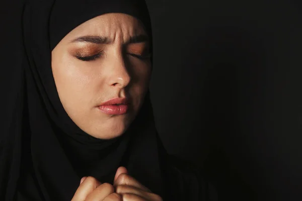 Portrait of sad Muslim woman in hijab  praying on dark background. Space for text
