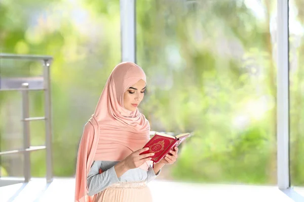 Muslim woman in hijab reading Koran indoors