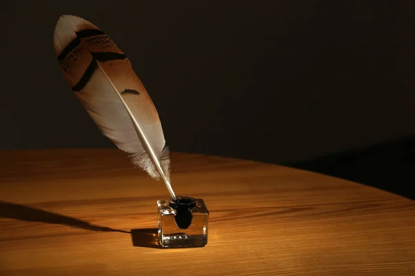 Feather pen and inkwell on wooden table in darkness. Space for text