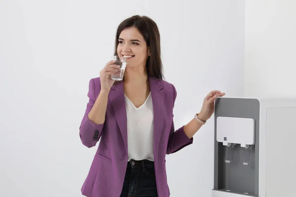 Young woman having break with glass of water near cooler in office