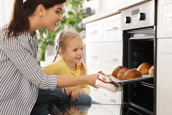 Mother and daughter taking out buns from oven in kitchen