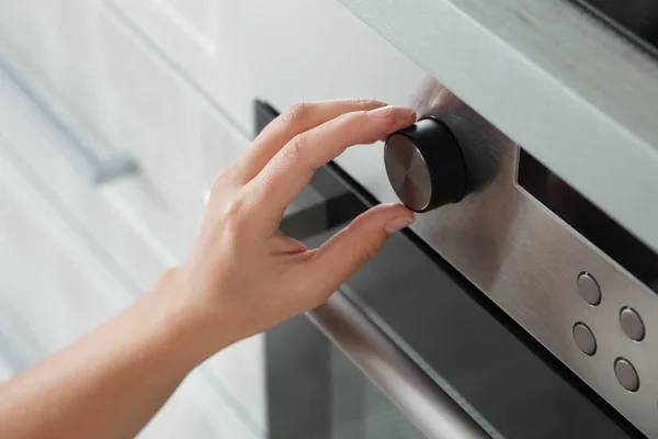 Woman regulating cooking mode on oven panel, closeup