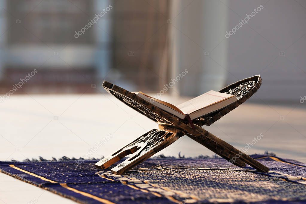 Rehal with open Quran on Muslim prayer mat indoors