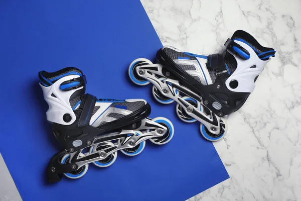Pair of inline roller skates on color background, top view