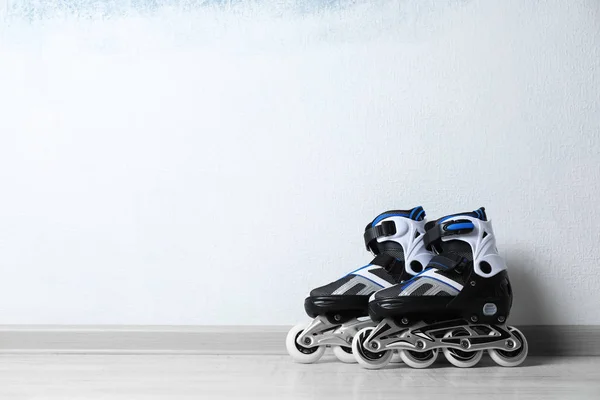Inline roller skates on floor near color wall. Space for text