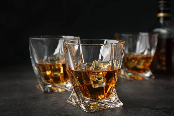 Golden whiskey in glasses with ice cubes on table