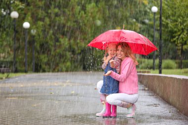 Mutlu anne ve kızı yağmurlu bir gün Park'ta kırmızı şemsiye ile. Metin için yer
