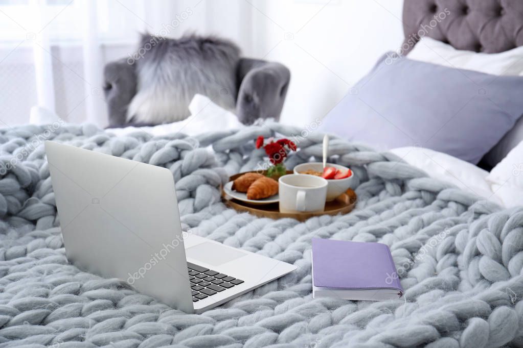 Laptop, notebook and tray with breakfast on bed in stylish room interior