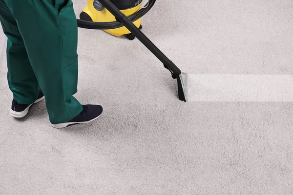 Man removing dirt from carpet with professional vacuum cleaner in room