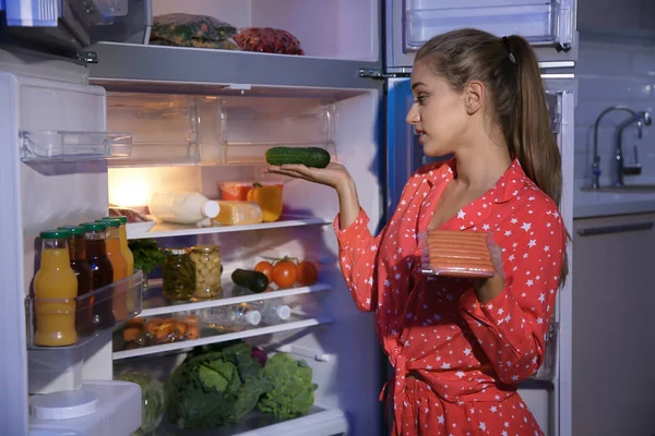 Young woman choosing food in refrigerator at night