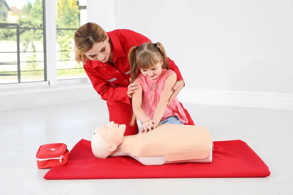 Instructor with little girl practicing first aid on mannequin indoors