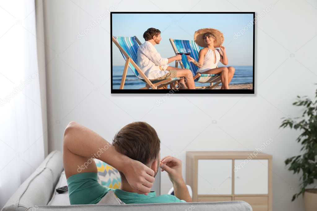 Young man watching TV on sofa at home