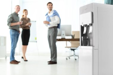 Cam ve arka plan üzerinde bulanık ofis çalışanları ile modern su soğutucu. Metin için yer