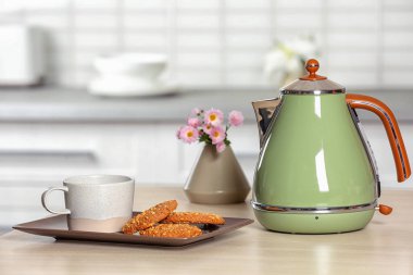 Şık elektrikli su ısıtıcısı, kupa ve bulanık odası iç karşı masada kurabiye. Metin için yer