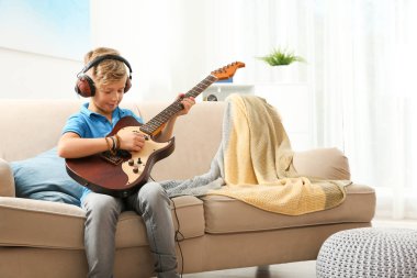 Sevimli küçük çocuk odasında kanepede gitar çalmak kulaklıklarla. Metin için yer
