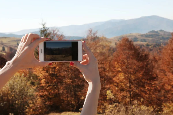 Woman taking photo of beautiful mountain landscape with smartphone