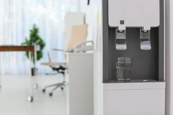 Modern water cooler with glass in office. Space for text