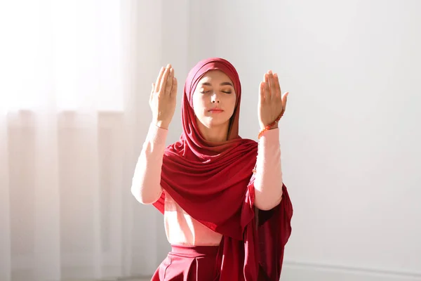 Young Muslim woman in hijab praying indoors