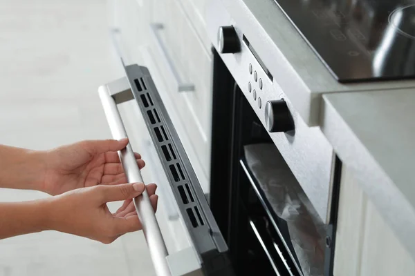 Young woman opening electric oven in kitchen, closeup