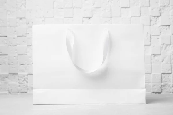 Paper shopping bag with ribbon handles on table near white wall. Mockup for design