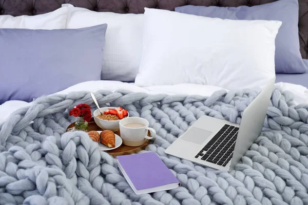Laptop, tray with breakfast and notebook on bed. Interior element