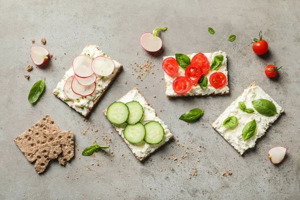 Tasty snacks with cream cheese and vegetables on gray table, flat lay