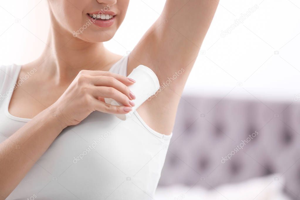 Beautiful young woman applying deodorant in bedroom. Space for text