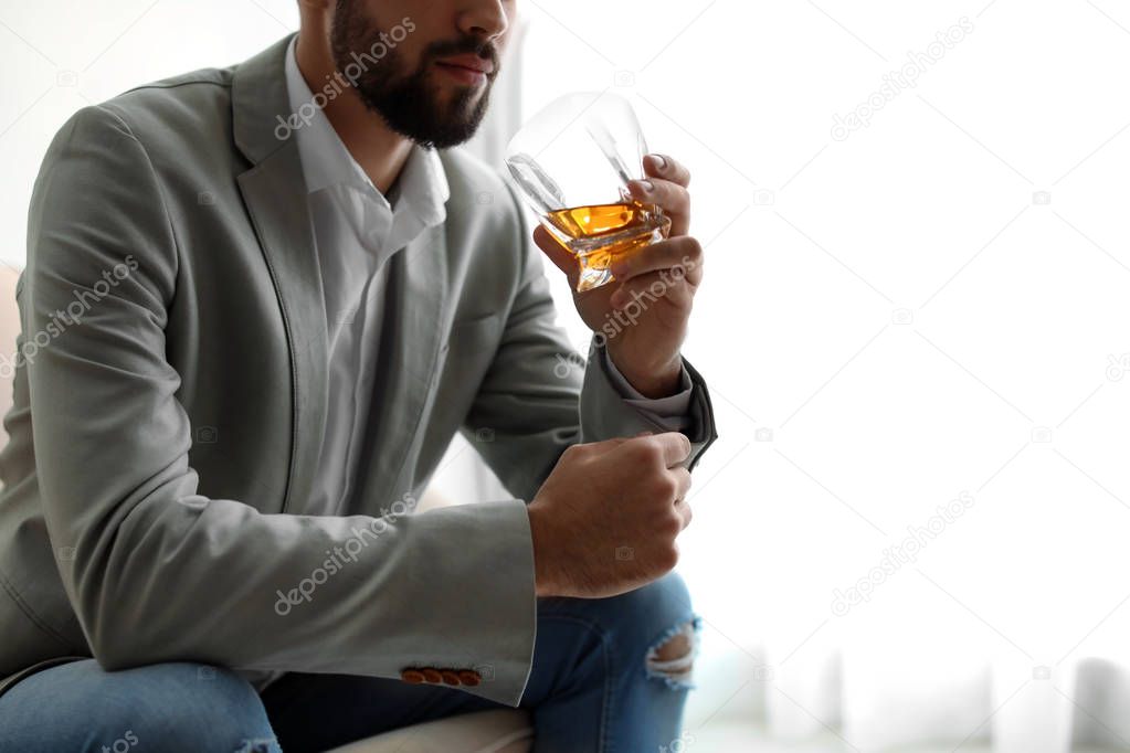 Young man with glass of whiskey at home, closeup. Space for text
