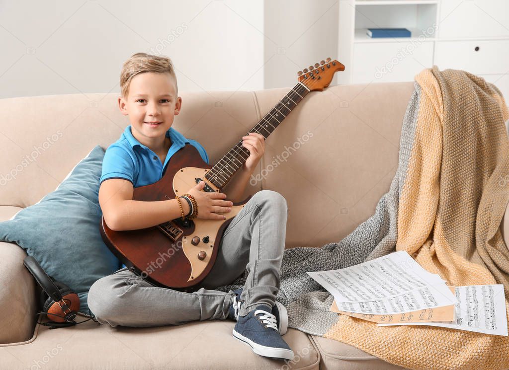 Cute little boy playing guitar on sofa in room. Space for text