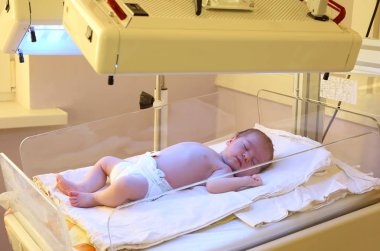 Newborn child under ultraviolet lamps in hospital clipart
