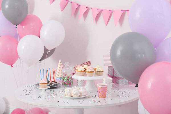 Party treats and items on table in room decorated with balloons