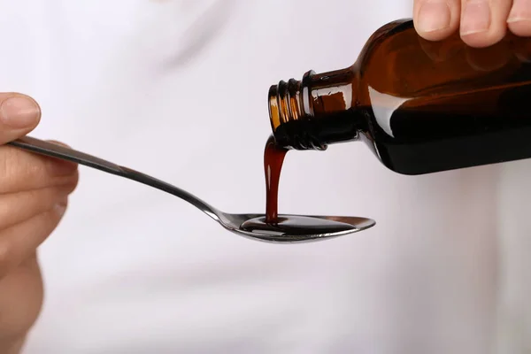 Woman pouring cough syrup into spoon, closeup