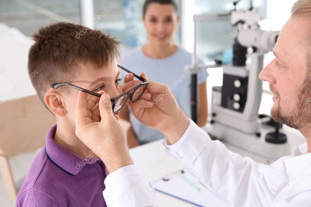 Children's doctor putting glasses on little boy in clinic