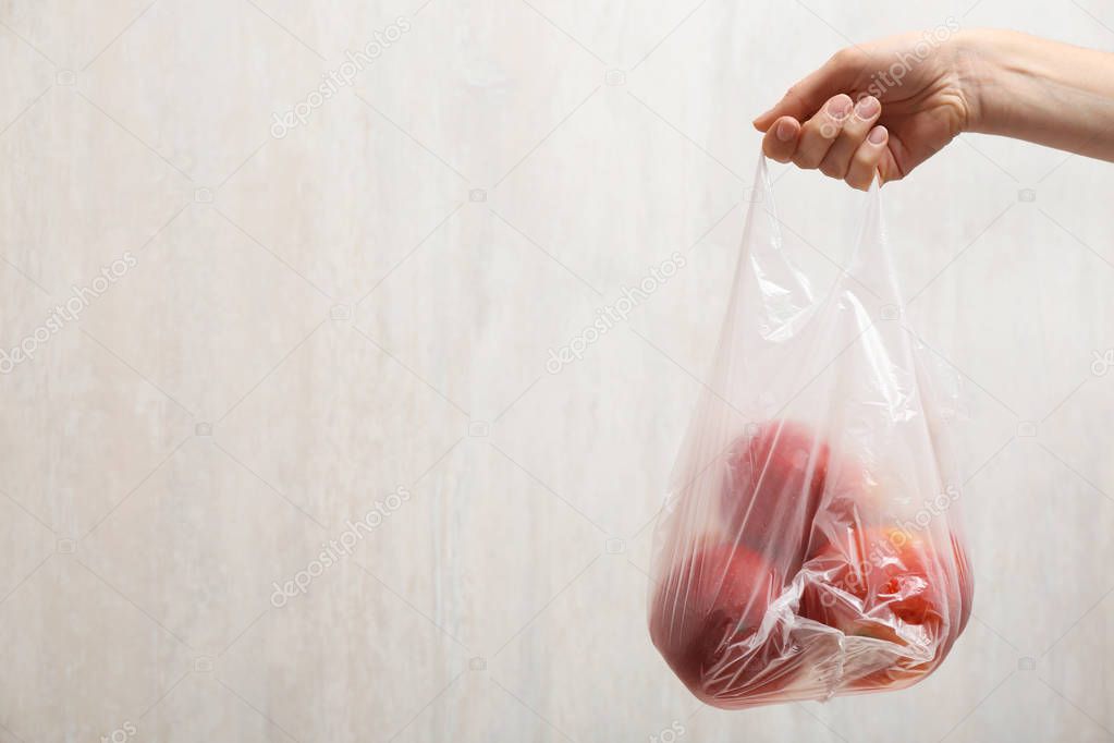 Woman holding plastic bag with apples on light background, closeup. Space for text