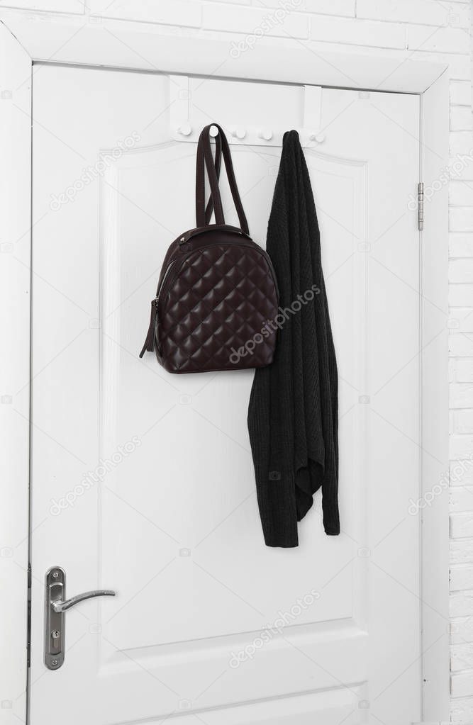 Backpack and clothing hanging on white wooden door