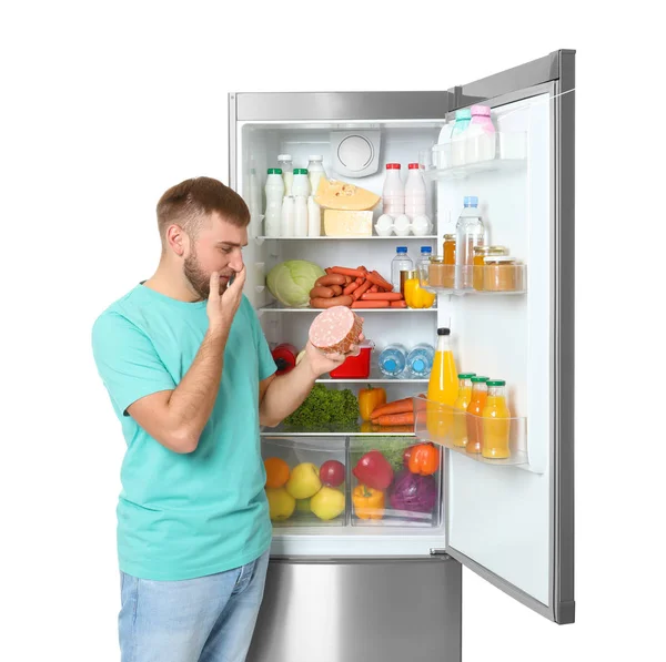 Молодой Человек Просроченной Колбасой Рядом Открытым Холодильником Белом Фоне — стоковое фото