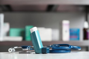 Asthma inhaler and stethoscope on table against blurred background clipart
