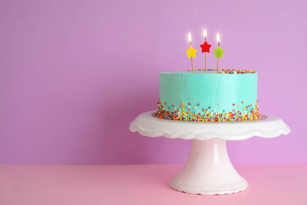 Свежий вкусный праздничный торт со свечами на стенде на цветном фоне. Пространство для текста

