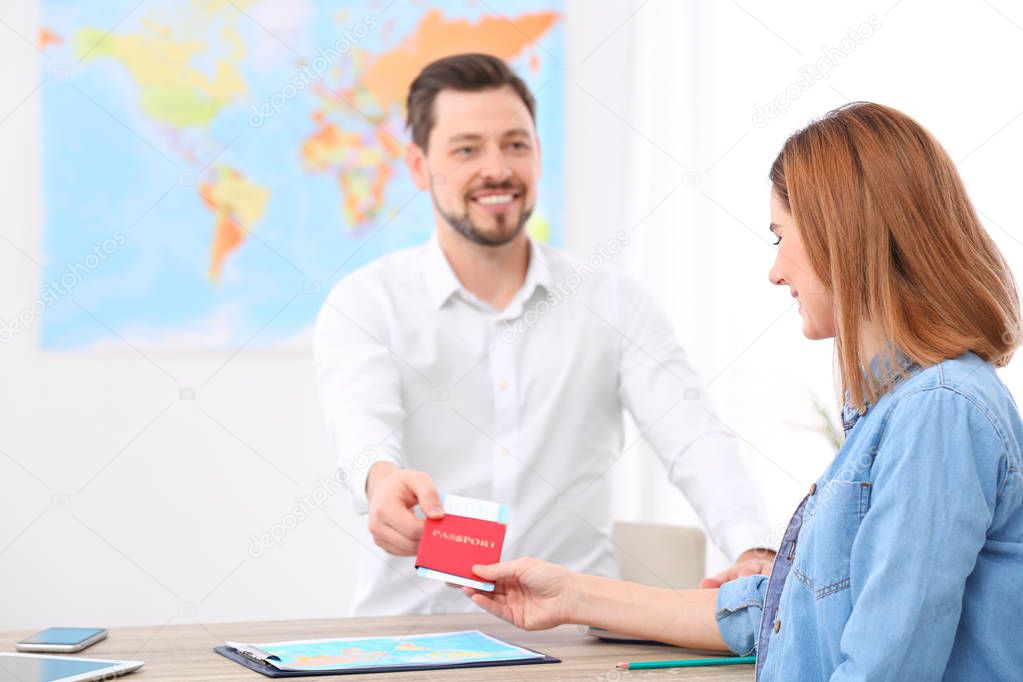 Male manager giving passport with ticket to client in travel agency