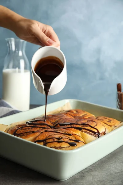 Woman Pouring Chocolate Syrup Freshly Baked Cinnamon Rolls Table Closeup — Stock Photo, Image
