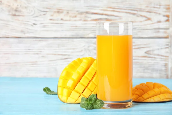 Glass with fresh mango juice and tasty fruits on wooden table. Space for text