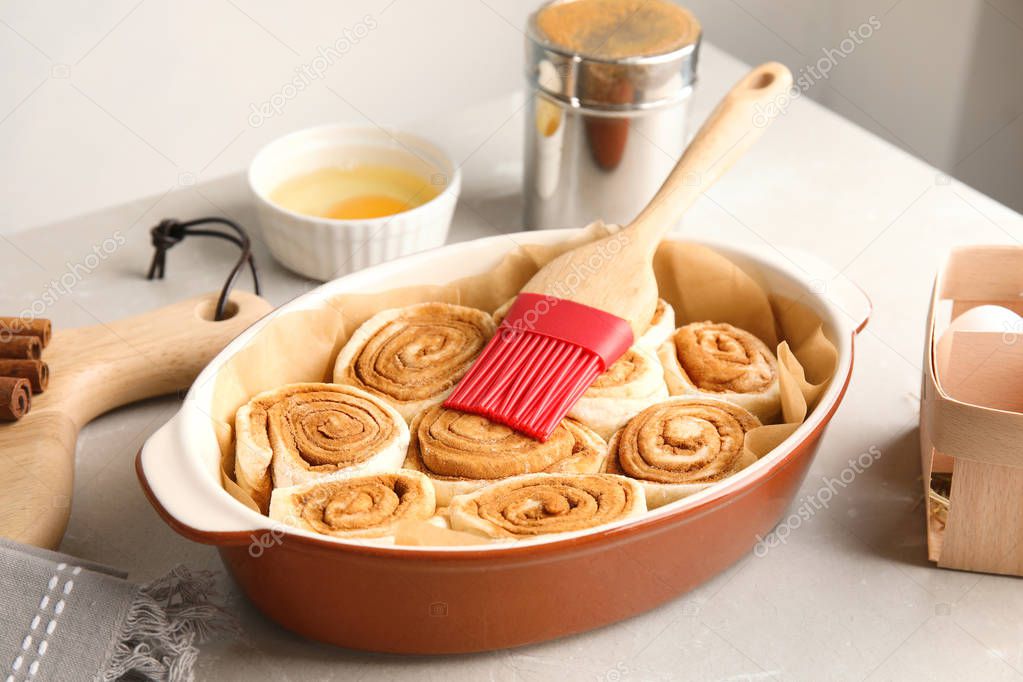 Baking dish with raw cinnamon rolls and pastry brush on table