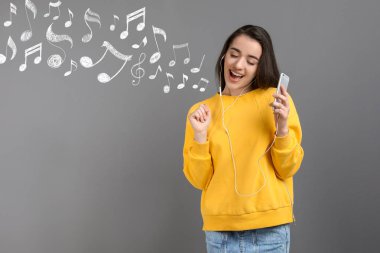 Genç kadın ile smartphone, kulaklık ve müzik notlar gri bir arka plana dayanır. Metin için yer