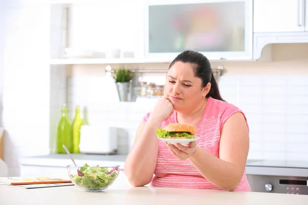 Θλιβερή Υπέρβαρη Γυναίκα Επιλέγοντας Ανάμεσα Σαλάτα Και Burger Στην Κουζίνα — Φωτογραφία Αρχείου